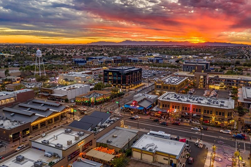 Aerial drone view of Gilbert, Arizona's Heritage District at sunset with the historic water tower, glowing city streets, and a vivid desert sky