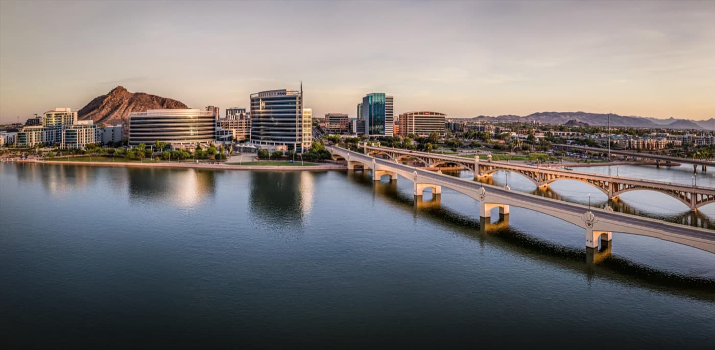 Tempe Town Lake at golden hour with the Mill Avenue Bridge reflected in calm water and the Tempe city skyline in the background